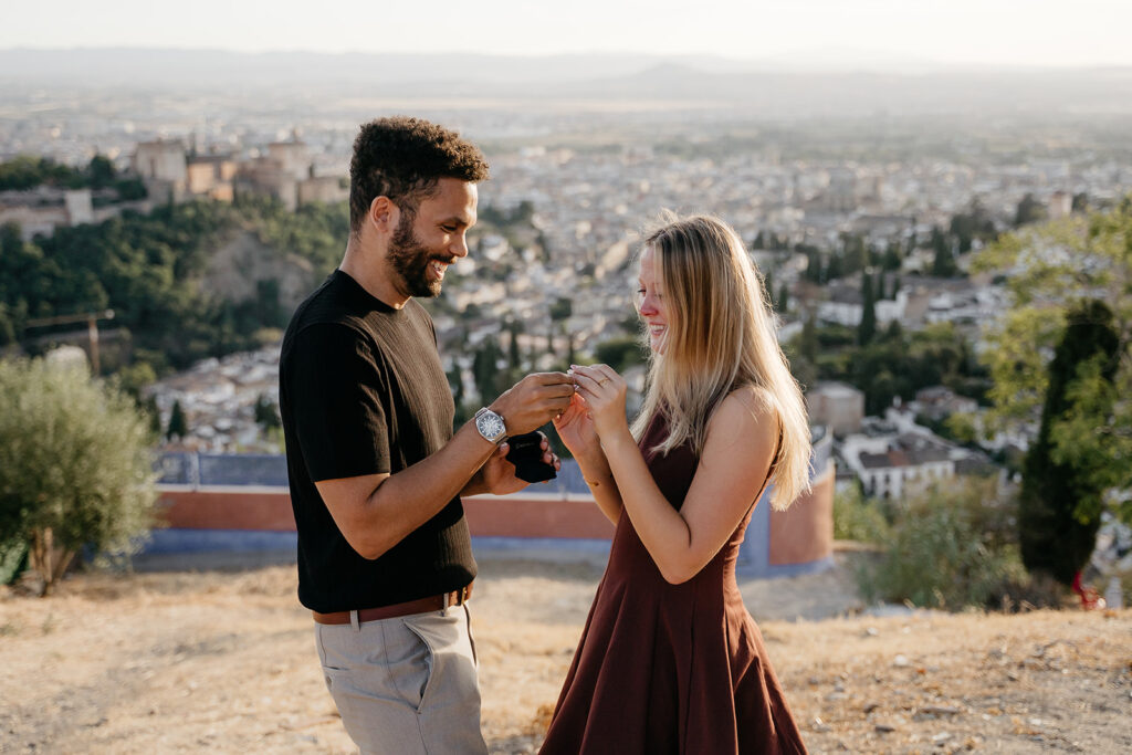 He slips the ring on her finger after a surprise proposal in Granada